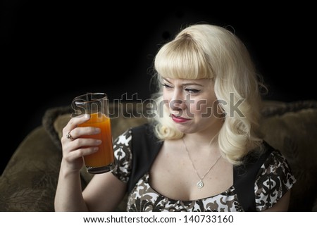Portrait of a beautiful young woman with blond hair drinking a glass of mango juice.