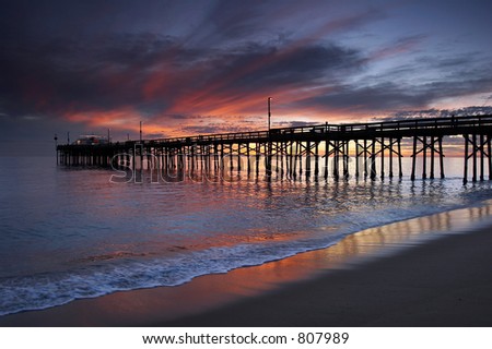 Old wooden pier at sunset with some people walking and fishing.