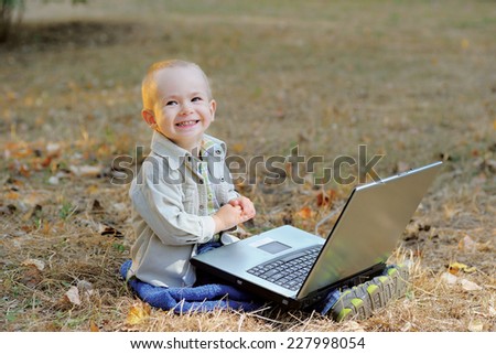 Smiling Child and Laptop/ A smiling little boy with a laptop on his legs, sitting on the ground in autumnal surrounding
