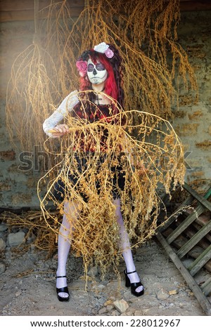 Gothic Beauty; A lady with Mexican mask on her face posing and holding a withered plant in her hands