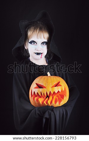 Gothic Little Beauty with Pumpkin; A little girl in a fancy dress with her face painted in Gothic/Vampire style holds Pumpkin