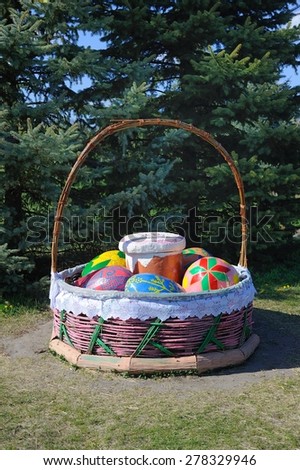 Huge Easter Basket/a gigantic basket with Easter eggs and bread in a park with trees behind
