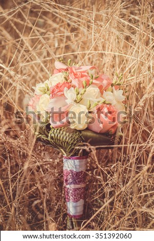 Bridal autumn bouquet with red and white roses over yellow autumn grass. Wedding in fall.