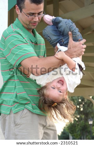 Father playfully holding his laughing daughter upside-down.