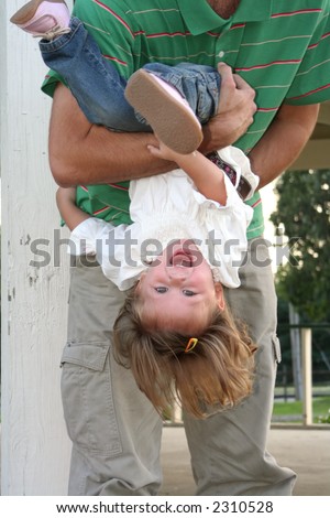 Laughing little girl playfully being held upside-down by her father.