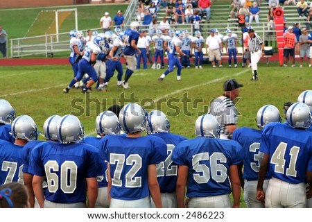 High school football team on the sidelines watching a game in progress.