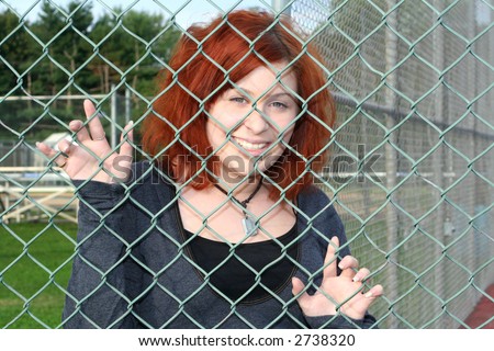 Smiling teen girl behind a chain link fence at a baseball field.