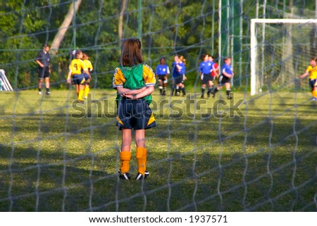 A goalie waits with crossed arms for the play to come to her end of the field.