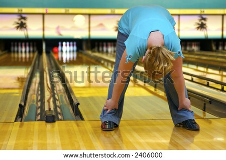 A young gal at the bowling alley - playing \'crazy bowl\' - a game where you do a variety of different ways of rolling the ball down the alley - like with your feet etc.