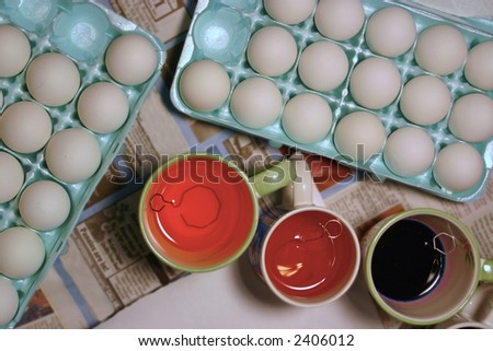 eggs sit in an egg tray waiting to be dyed - the dye is in cups right next to the trays - unique view from directly above.