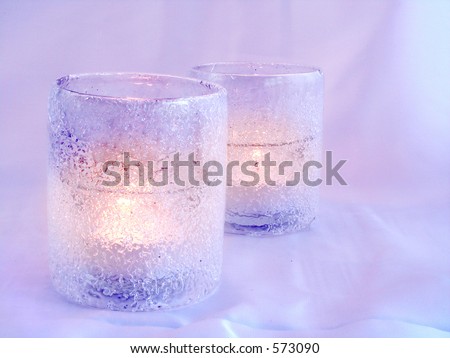 Picture of two frosted candle-holders with burning candles on a soft colored background.