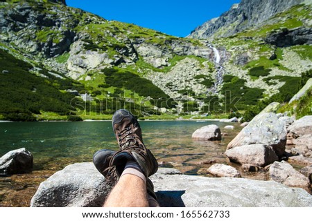 Hiker resting over the glacier lake with a waterfall in the background in high mountains. Taken in High Tatras, Slovakia, Europe.