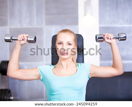 Attractive blond   sporty girl doing shoulders training with a dumbbell
