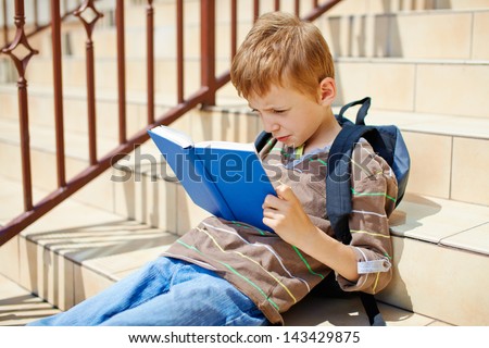 Young boy reading book on school stairs