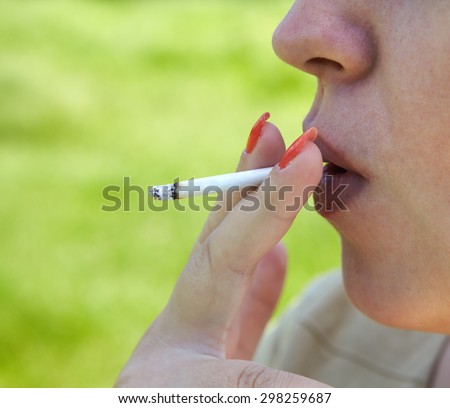 Mouth with red lips and red finger nails smoking cigarette