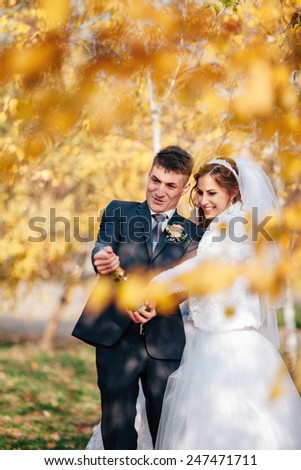 Wedding couple open champagne in the autumn park