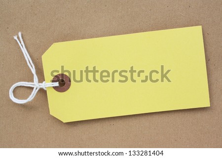 Blank yellow paper luggage tag or price tag on a brown parcel paper background