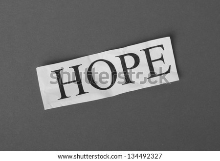 A black and white photograph of the word Hope typed on a scrap of crumpled white paper resting on a dark, textured paper background