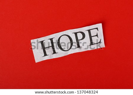 The word HOPE typed out on a scrap of crumpled paper against a red textured paper background