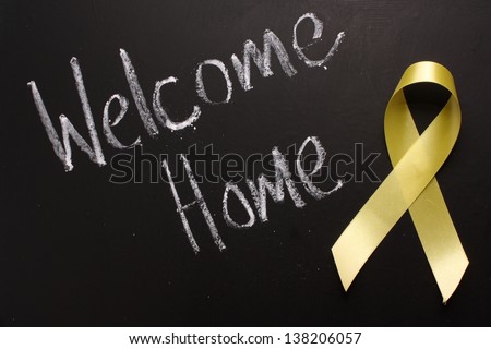 The words Welcome Home written on a blackboard next to a yellow ribbon,in reference to military returning from overseas duty.