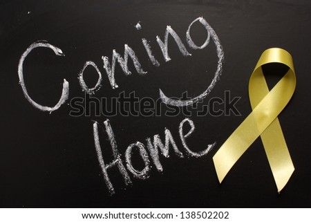 The words Coming Home written on a blackboard next to a yellow ribbon, in reference to military returning from overseas duty.