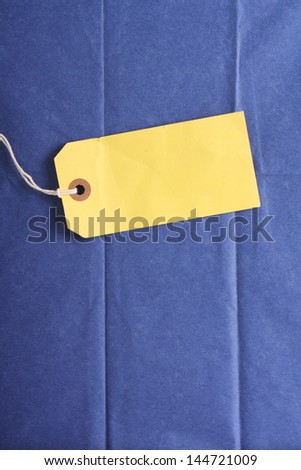 Blank yellow paper luggage or gift tag on a background of blue tissue wrapping paper