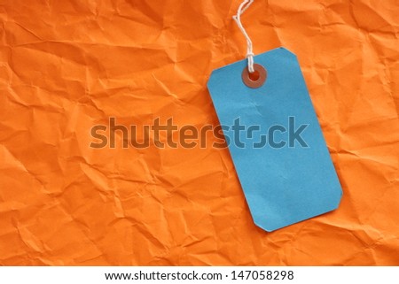 Blue paper luggage or price tag on a background of wrinkled orange paper with room for your text