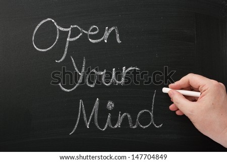 A hand writing Open Your Mind on a blackboard. A concept for having an open mind to new ideas,experiences and opportunity in our careers, education and personal lives