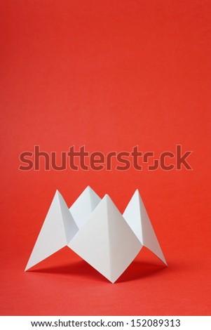 An origami fortune teller or cootie catcher made from blank white paper on a red background with room for your text.