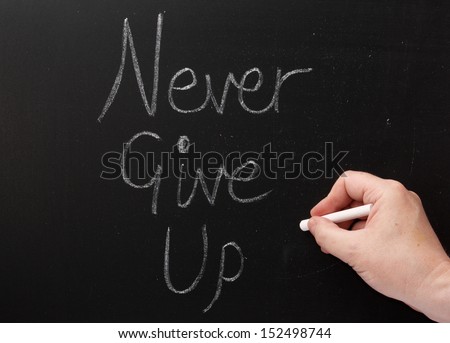 Hand writing the words Never Give Up on a blackboard with white chalk. One of the secrets or keys to success.