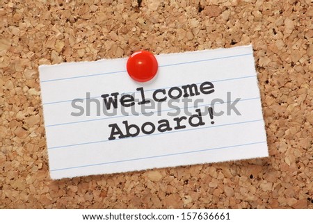 The phrase Welcome Aboard! typed onto a scrap of lined paper and pinned to a cork notice board. A phrase used to welcome a new employee or team member.