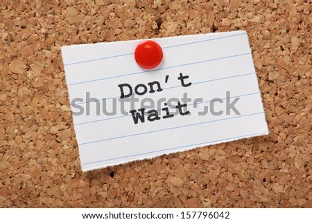 Don\'t Wait typed onto a scrap of lined paper and pinned to a cork notice board. A call to take action and get things as opposed to wasting time and procrastination.