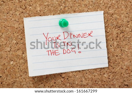 Your Dinner is in the Dog written on a paper note pinned to a cork notice board. A humorous concept for relationship difficulties and living life as a married or common law couple.