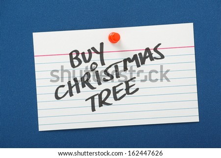 A reminder to buy a Christmas Tree written on a white note card pinned to a blue notice board.