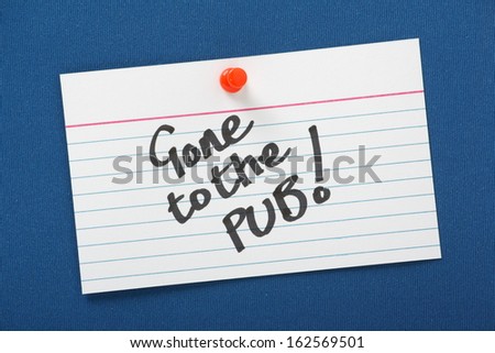 A white note card with the message Gone To The Pub written on  it and pinned to a blue notice board.