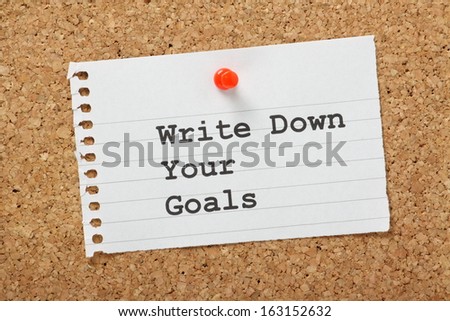 Write Down Your Goals typed on a scrap of paper pinned to a cork notice board. Writing down goals helps to make them more real and will provide focus as you plan the steps to reach them.