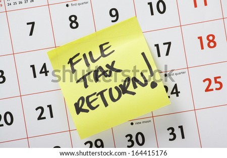Hand Written Reminder To File Tax Return On A Yellow Post It Note Stuck To A Calendar Background