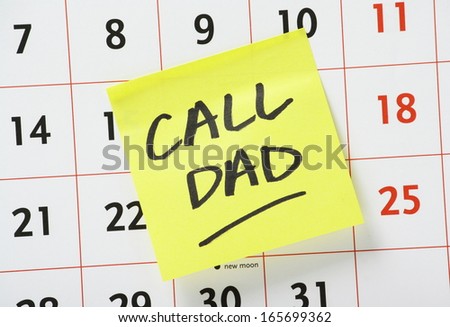 The phrase Call Dad written on a yellow sticky paper note and stuck to a wall calendar.