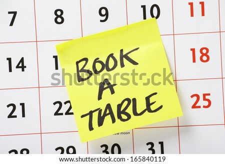 A reminder to book a table or make a reservation for dinner on a yellow paper sticky note stuck to a wall calendar background