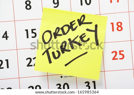 Reminder to Order a Turkey in time for Christmas dinner written on a yellow sticky paper note stuck to a wall calendar background