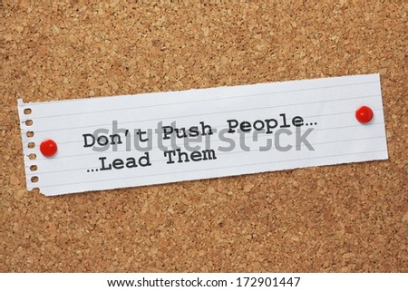 The phrase Don\'t push People, Lead Them on a paper note pinned to a cork notice board. A concept for leadership being used to motivate people.