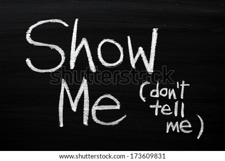 The phrase Show Me, Don\'t Tell Me written by hand in white chalk on a used blackboard. Often used in business but more so as a guide for novel and book writers.