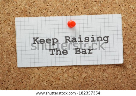 The phrase Keep Raising the Bar on a piece of graph paper pinned to a cork notice board. A concept for raising standards and setting targets as a form of motivation.