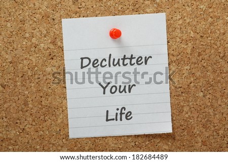 The phrase declutter your life typed on lined paper and pinned to a cork notice board. The process of removing unnecessary distraction drives productivity and efficiency at work and at home.