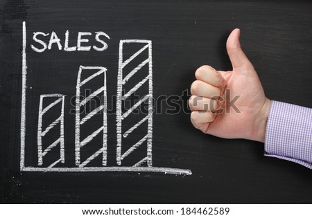 A graph showing Sales rising on a blackboard with a hand in a business shirt giving the okay thumbs up
