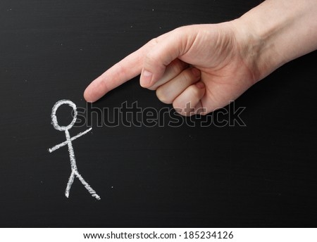 A giant hand pointing the index finger at a chalk stick figure on a blackboard