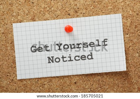 The phrase Get Yourself Noticed typed on a piece of graph paper and pinned to a cork notice board