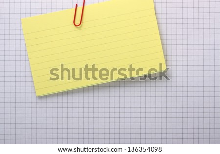 A yellow index card clipped with a paperclip to a grey lined sheet of graph paper with copy space