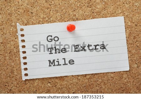 The phrase Go The Extra Mile typed on a piece of lined note paper and pinned to a cork notice board