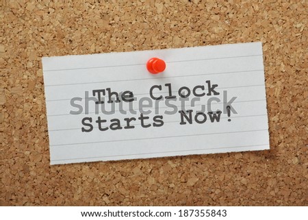 The phrase The Clock Starts Now typed on a piece of lined paper and pinned to a cork notice board